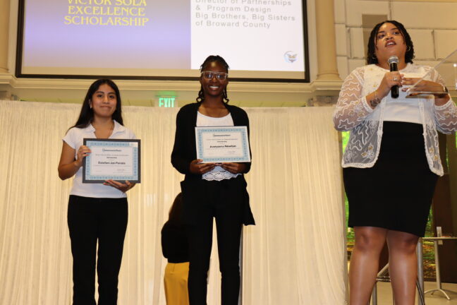 Woman giving a speech with the excellence scholarship winners